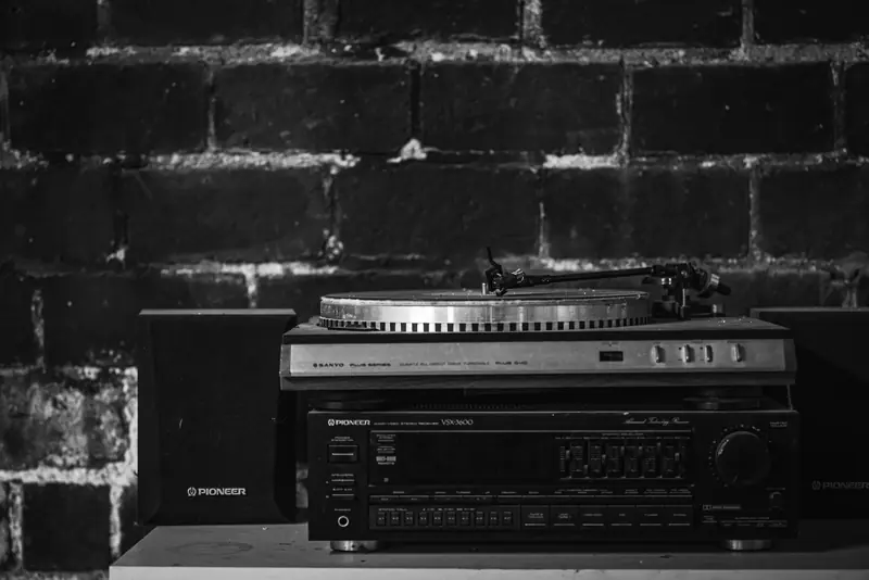 Monochrome image of a vintage turntable and audio setup with speakers against a brick wall