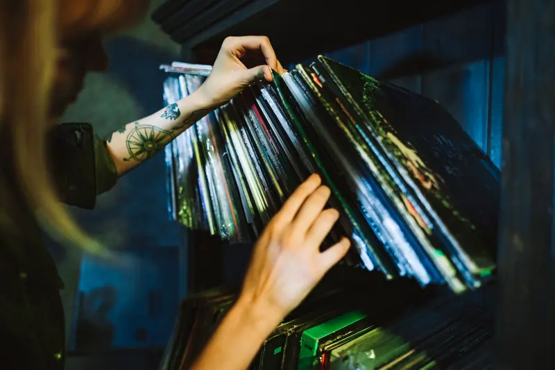 Close-up of a woman picking vinyl records from a shelf with a tattooed arm