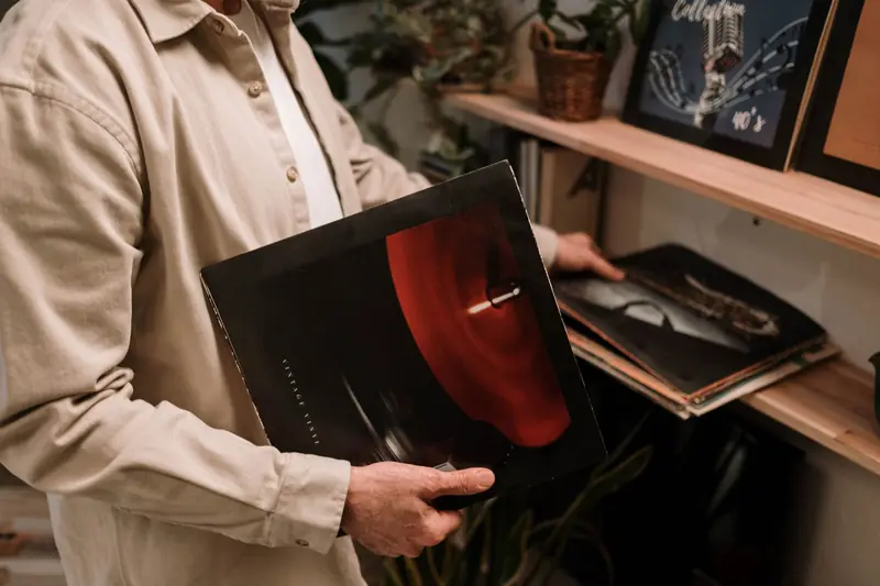 Adult holding vintage vinyl record, browsing a collection on a shelf indoors