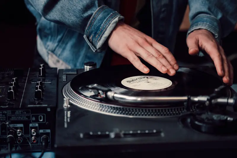 DJ mixing vinyl records on a turntable, creating live music with a sound mixer