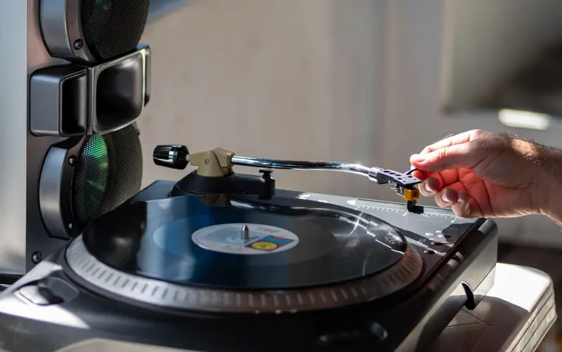 Close-up of a hand adjusting a needle on a vintage vinyl turntable next to speakers